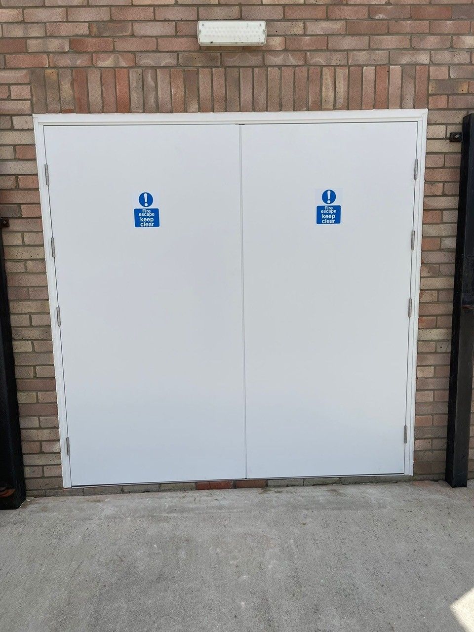 White fire door with blue signs on a brick wall
