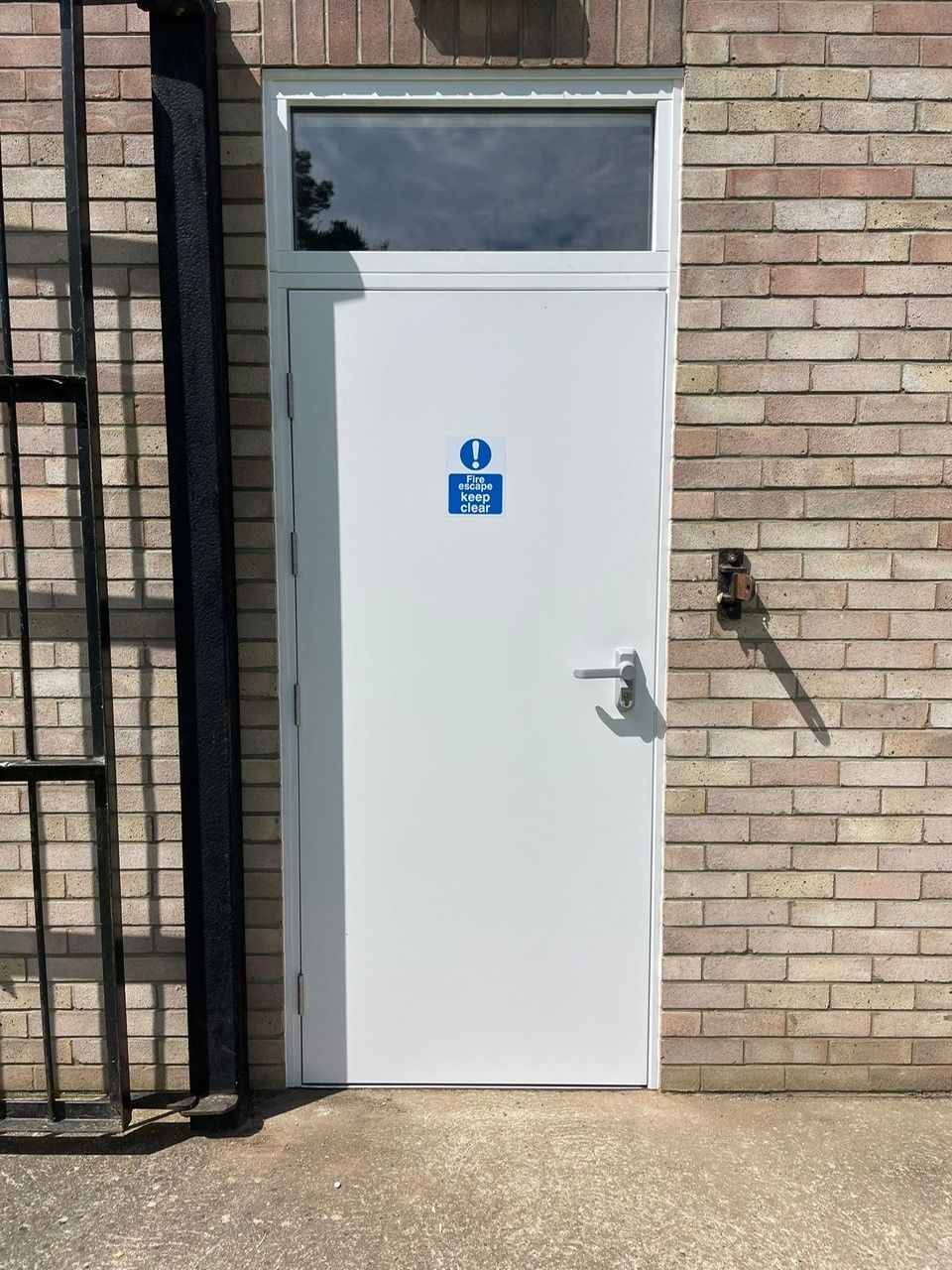 White fire rated door with a blue sign on a brick wall