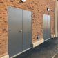 Two gray fire rated doors on a brick building with a dark asphalt driveway.